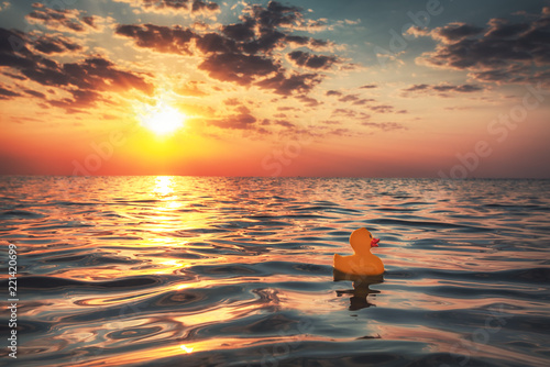 Yellow rubber duck toy floating in sea water. Beautiful sunrise on the beach.