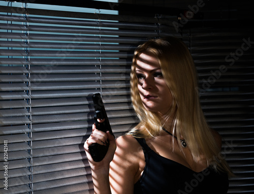 Wallpaper Mural A young woman with a gun is standing by the window with jalousie Torontodigital.ca