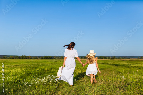 rear view of mother and daughter walking together by green field on sunny day