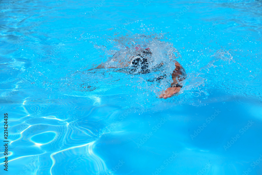 Caucasian man swims in freestyle (crawl) at the outdoor swimming pool on a sunny summer day
