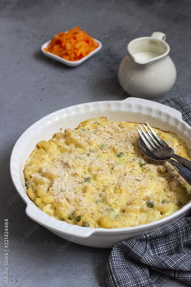 Homemade pasta casserole with fish and green pea in bechamel sauce in a baking dish on a light slate, stone or concrete background. Copy space for text. Homemade pasta casserole with fish and green pea in bechamel sauce in a baking dish on a light slate, stone or concrete background. Copy space for text.