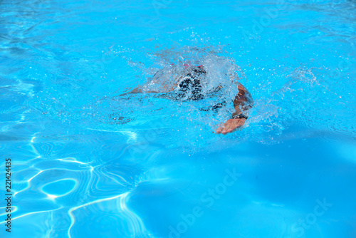 Caucasian man swims in freestyle (crawl) at the outdoor swimming pool on a sunny summer day © Stefania
