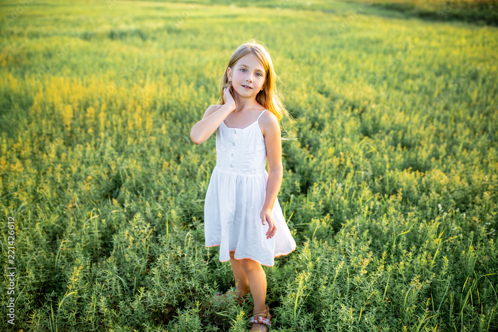 cute little child in white dress posing on field and looking at camera cute little child in white dress posing on field and looking at camera