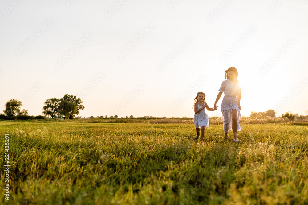mother and daughter walking in green meadow with sunset on background mother and daughter walking in green meadow with sunset on background