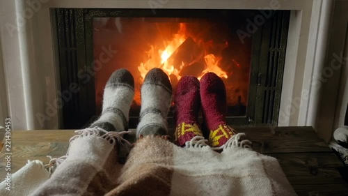 Slow motion video of roamntic couple lying under blanket and warming feet by burning fireplace at night photo