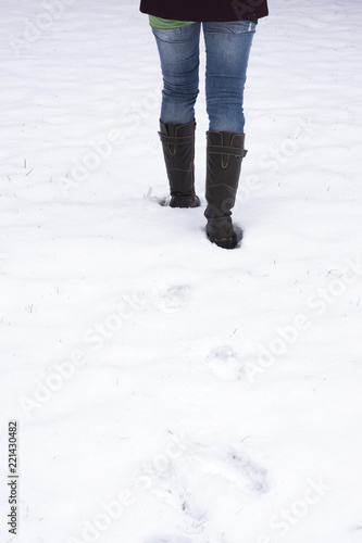 rear view of woman walking through snow leaving behind footprints