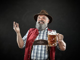 Germany, Bavaria, Upper Bavaria. The smiling man with beer dressed in in traditional Austrian or Bavarian costume in hat holding mug of beer at studio