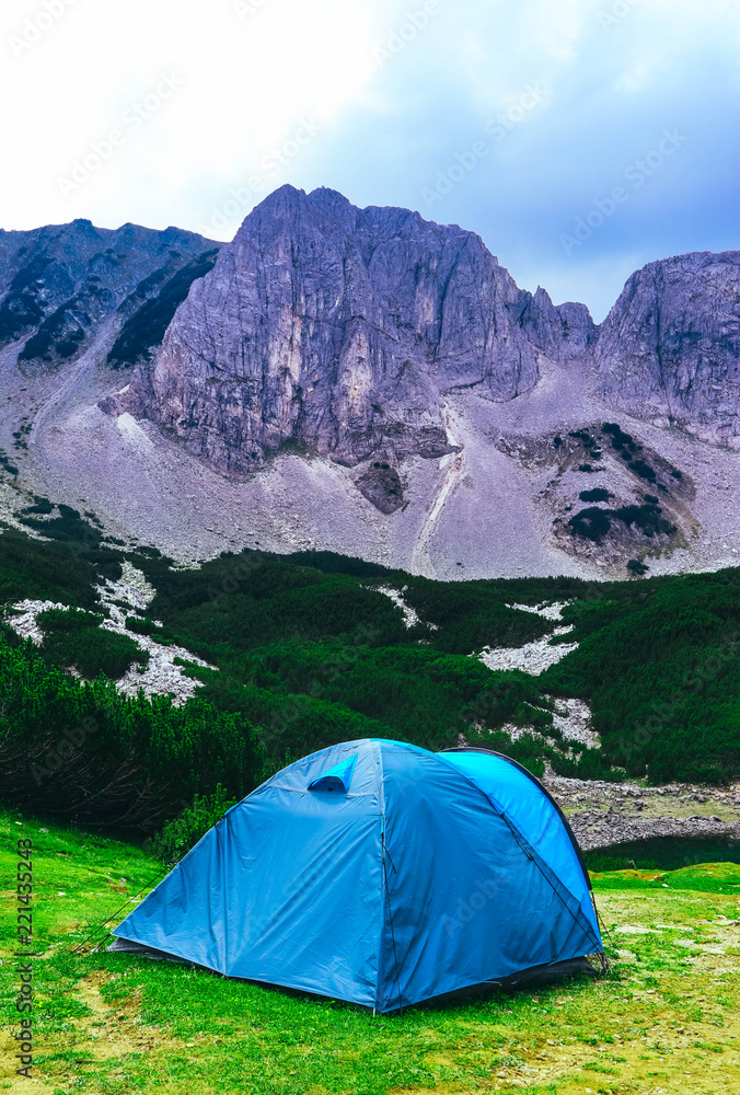 Blue сamping tent in the alpine mountains, summer time. Hiking adventure concept.