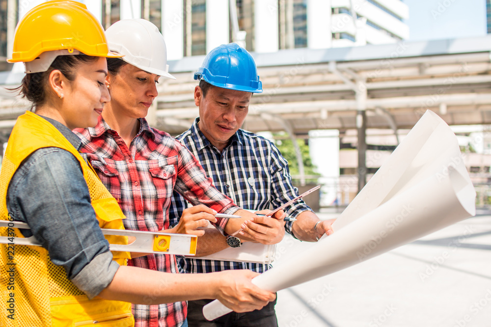 Three industrial engineer wear safety helmet engineering working and talking with drawings inspection on building outside. Engineering tools and construction concept. Three industrial engineer wear safety helmet engineering working and talking with drawings inspection on building outside. Engineering tools and construction concept.