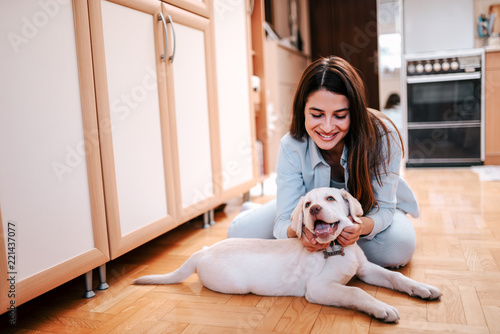 Beautiful young woman caressing her pet while sitting on the floor at home. photo