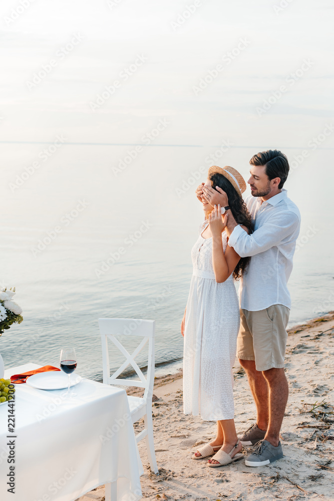 young man closing eyes and making surprise for girlfriend, romantic date on beach