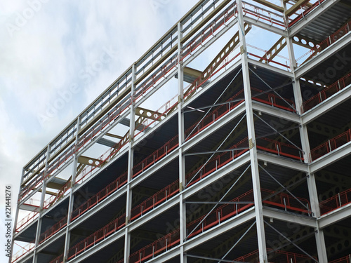 angled view of a large building development under construction with steel framework and girders supporting the metal floors with blue sky and clouds