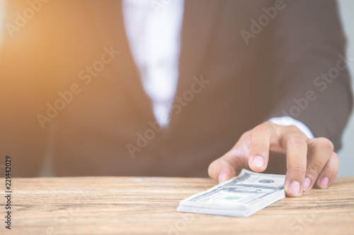 Close up hand of businessman holding money dollar bills on wooden table. Using as concept of corruption , Business corruption, bribe. With copy space for your text.