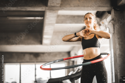 Beautiful caucasian young woman doing hula hoop in step waist hooping forward stance. Young woman doing hula hoop during an exercise class in a gym. Healthy sports lifestyle, Fitness, Healthy concept. photo