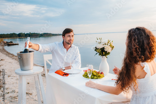 handsome man taking bottle of champagne for romantic date on beach