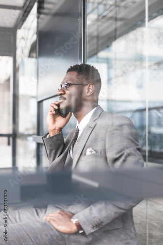 black man businessman in a business suit, expensive watch and glasses talking on the phone, decides business matters against the backdrop of a modern city to work