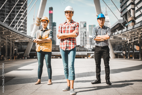 Three Industrial engineer wear safety helmet engineering standing with arms crossed holding inspection tablet and smile on building outside office. Engineering tools and construction concept.