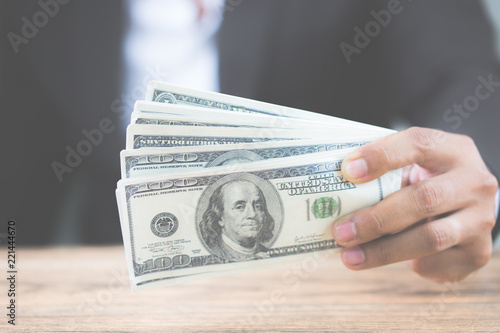 Close up hand of businessman holding money dollar bills on wooden table. Using as concept of corruption , Business corruption, bribe. With copy space for your text.