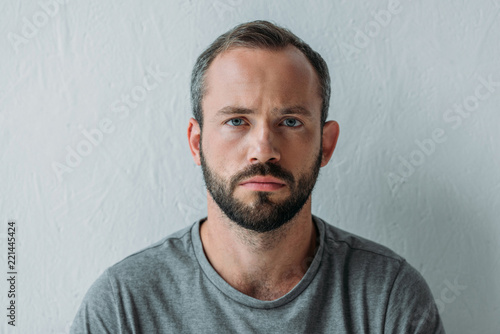 Bild auf Leinwand portrait of unhappy bearded man looking at camera on grey
