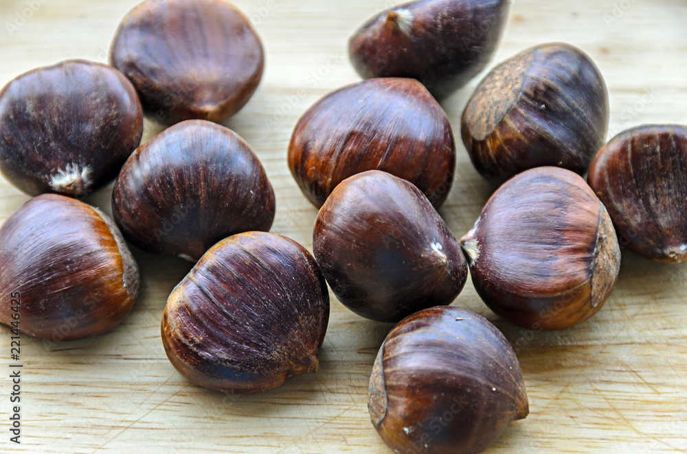 Fototapeta premium Edible brown chestnuts close up, wooden background