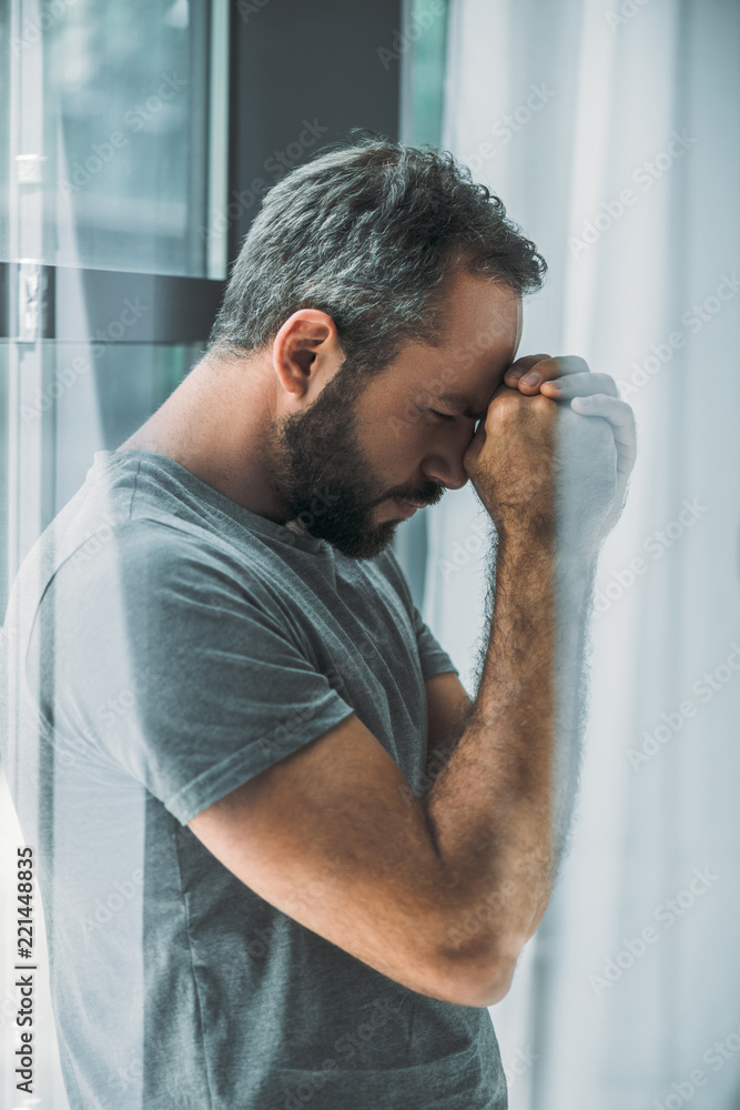 side view of depressed frustrated bearded man standing near window - obrazy, fototapety, plakaty 