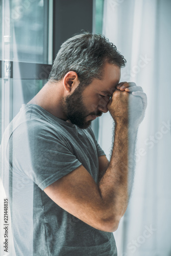 Konstfotografi side view of depressed frustrated bearded man standing near window