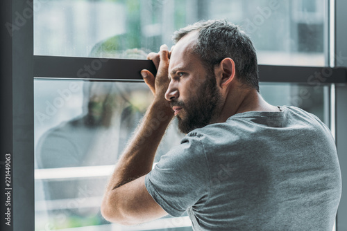 Bild auf Leinwand upset bearded man leaning at window and looking through it