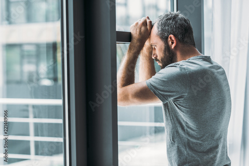 depressed bearded man leaning at window and looking through it