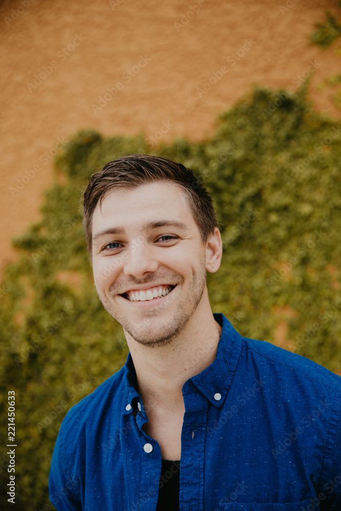 Attractive Male Model in Blue Collared Shirt in front of Orange Textured Vine Wall Attractive Male Model in Blue Collared Shirt in front of Orange Textured Vine Wall