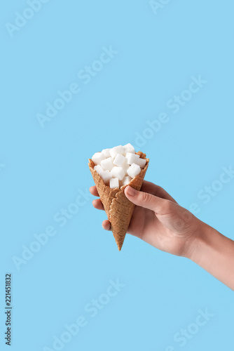 woman holding in hand ice-cream wafer cone filled with white sugar cubes isolated on blue background
