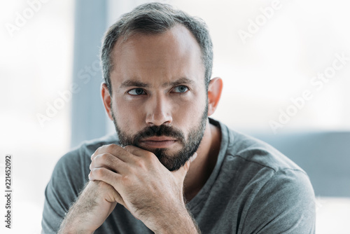 portrait of unhappy bearded middle aged man with hands on chin looking away