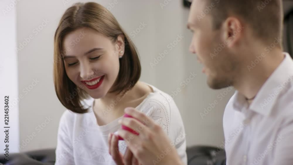 Two young people is sitting in a cafe. Man and woman are smiling and sitting in the cafe at the table during break. Couple is talking and drinking coffee. He proposes marriage Two young people is sitting in a cafe. Man and woman are smiling and sitting in the cafe at the table during break. Couple is talking and drinking coffee. He proposes marriage