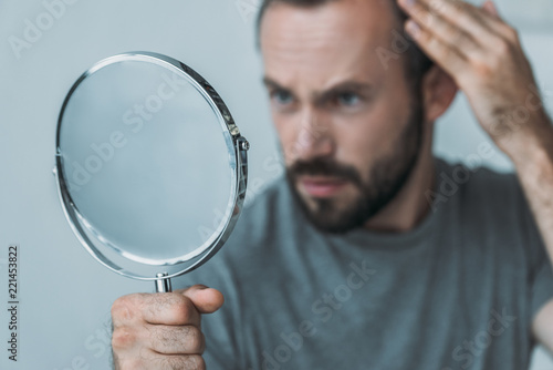 close-up view of bearded mid adult man with alopecia looking at mirror, hair loss concept