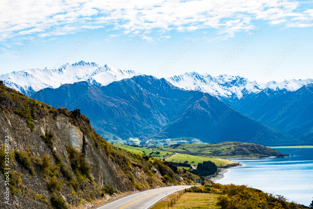 Stunning beautiful view of the road beside Lake Wanaka with alps mountain. Noon scenery with some cloudy and blue sky. nature scene in the countryside with green grassland and agriculture.