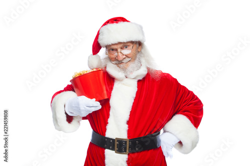 Christmas. Smiling, kind Santa Claus in white gloves holds a red bucket with popcorn with one hand, and puts the other hand on his belt. The concept of visiting the cinema, watching a movie with