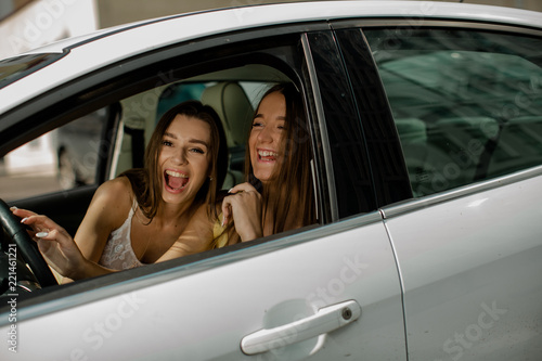 Two young beautiful girls rejoice in the car in the summer. A friendly trip of two girls © irinanillu