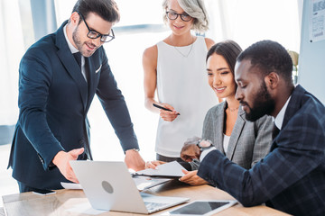 happy multicultural businesspeople working on project in office and looking at laptop
