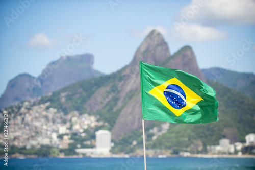 Brazilian flag flying in front of a bright view of Ipanema Beach with Two Brothers Mountain in Rio de Janeiro, Brazil