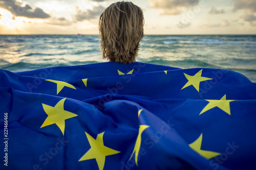 Man holding a fluttering iconic EU flag with circle of stars on beach at sunrise