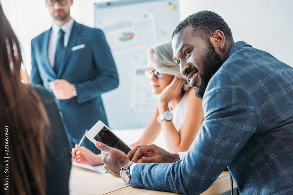 smiling african american businessman holding tablet and looking at colleague in office smiling african american businessman holding tablet and looking at colleague in office