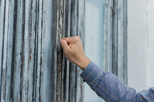 hand postman in a plaid shirt knocking his fist at the old and shabby front door Fototapete