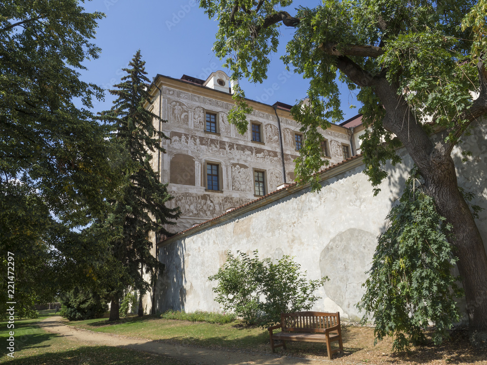 Renaissance style castle with Sgraffito decorated facade, park, footpath, green trees garden and wooden bench, sunny summer day