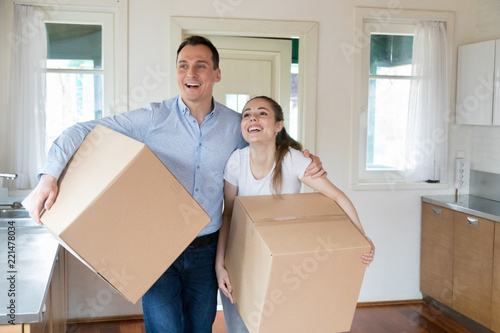 Excited man and woman enter room hugging carry cardboard boxes into new house, happy couple bring in carton packages with personal belongings smiling relocating to own apartment. New beginning concept © fizkes