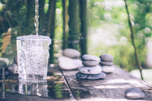 Clean water pouring into the glass next to the stones on the old wooden table. Japanese style. Cleansing and detox concept photo
