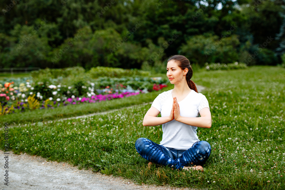 Fitness and yoga concept. Positive girl in a white t-shirt and blue  leggings doing yoga in the Park. Portrait on the background of nature. Woman  meditating Stock Photo | Adobe Stock
