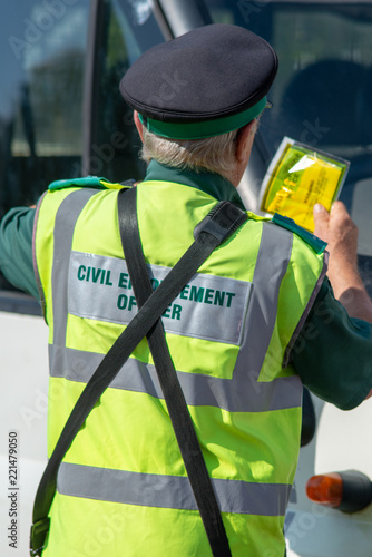 traffic warden civil enforcement officer wearing reflective yellow vest issuing fixed penalty parking ticket fine to white van