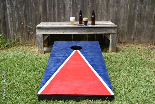 Red, white and blue corn hole game in back yard with dusty bags landing on board
