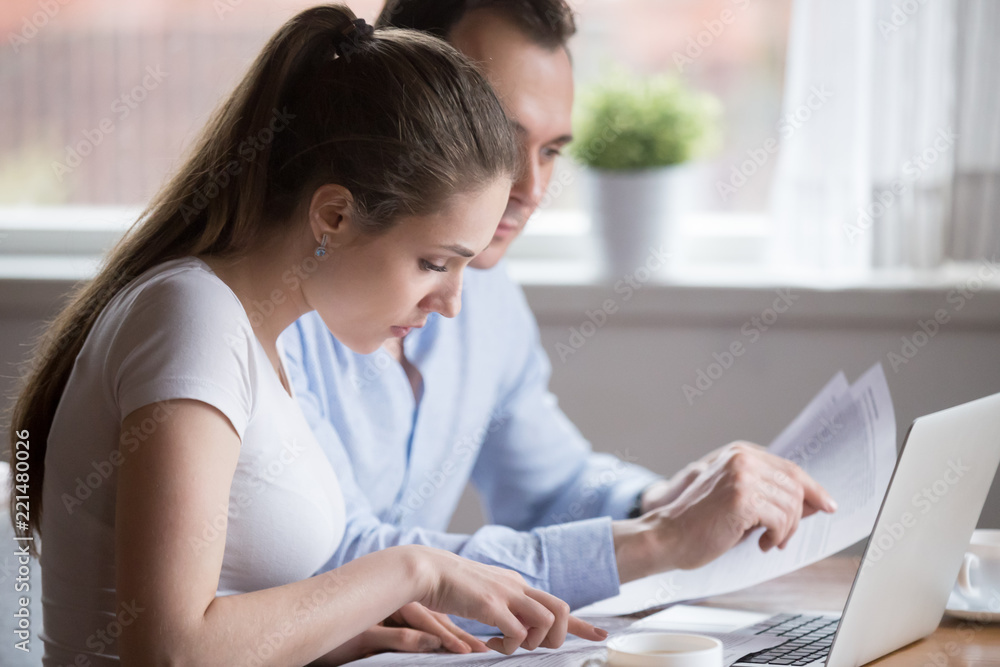 Serious millennial couple read documents managing house utility bills, man and woman analyze bank notice or insurance considering terms, husband and wife hold papers calculating finances or budget Serious millennial couple read documents managing house utility bills, man and woman analyze bank notice or insurance considering terms, husband and wife hold papers calculating finances or budget