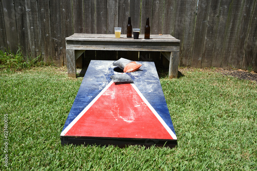 Red, white and blue corn hole game in back yard with dusty bags landing on board