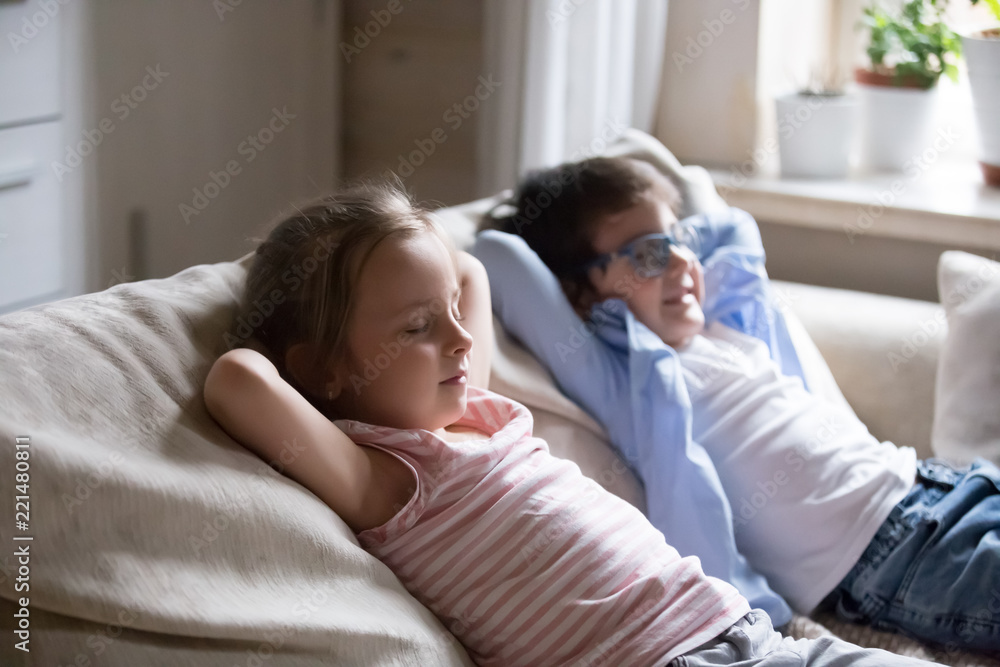 Cute little kids lying with eyes closed on cozy couch hands over head, little boy and girl taking nap relaxing on comfortable sofa in living room, funny siblings act like adults copying parents rest Cute little kids lying with eyes closed on cozy couch hands over head, little boy and girl taking nap relaxing on comfortable sofa in living room, funny siblings act like adults copying parents rest